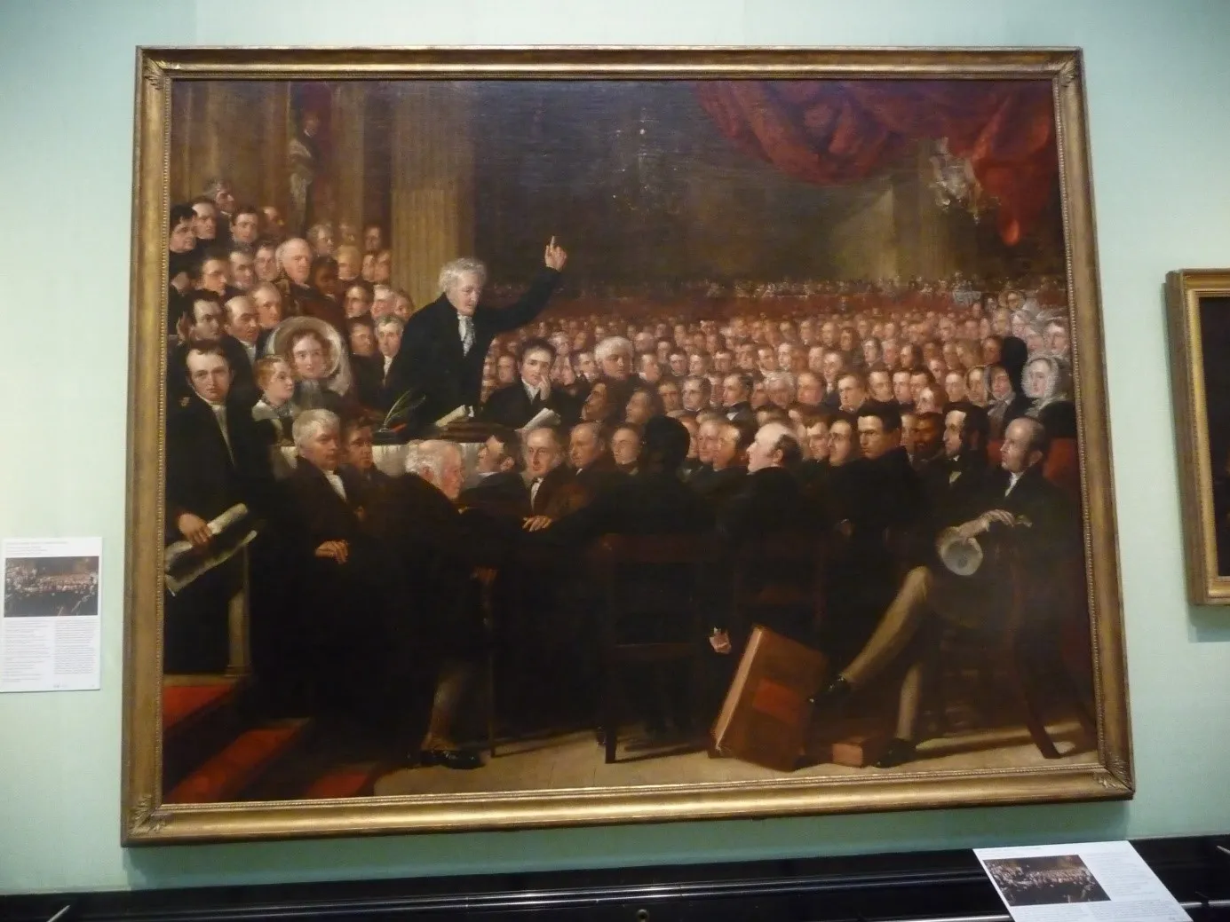 Peinture d'une réunion de François guizot, il se tient au dessus d'une foulle qui l'écoute attentivement